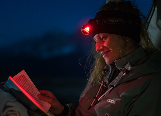 Eine Frau liest im Dunkeln mit einer Stirnlampe mit rotem Licht