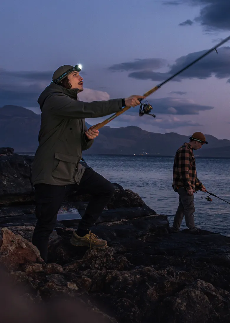 Two anglers wearing Ledlenser headlamps on a rocky coast at dusk