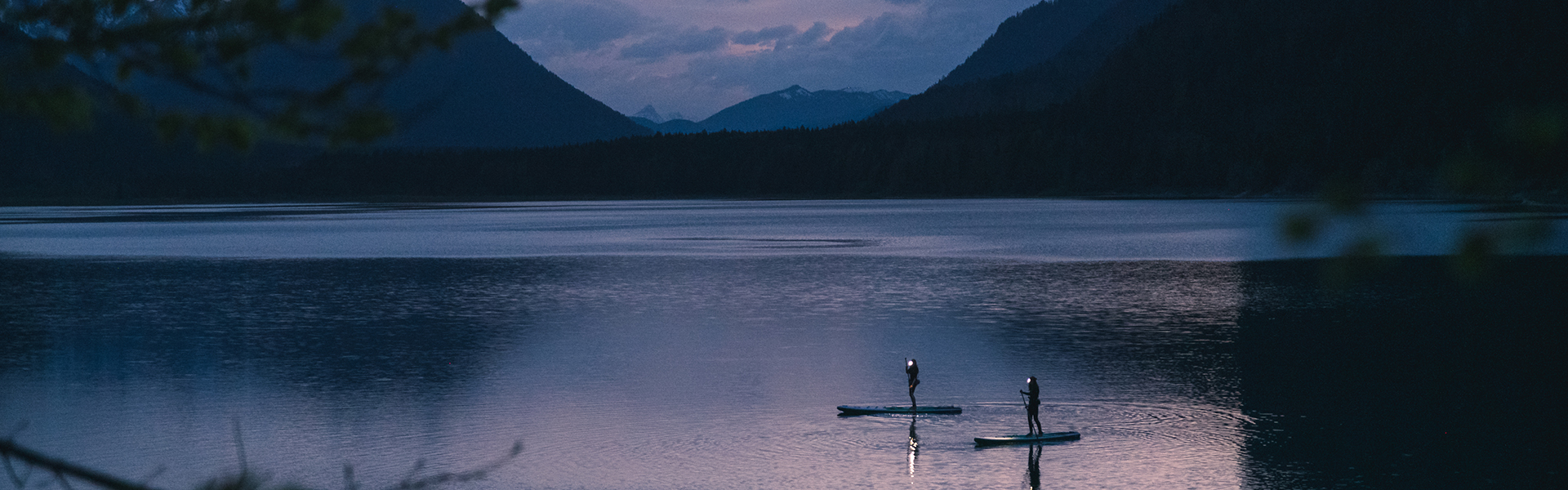 Zwei Standup-Paddler sind mit wasserdichten Stirnlampen auf dem Wasser.