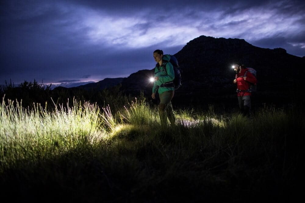 A man and a woman doing a night hike with flashlights and headlamps